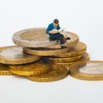 A miniature person sat atop a pile of gold coins
