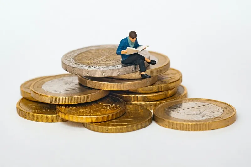 A miniature person sat atop a pile of gold coins