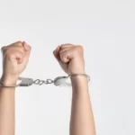 two hands handcuffed against plain background - crime and deviance in functionalism