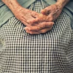 An older person with their hands in their lap