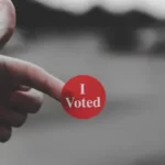 A finger holding a sticker saying 'I Voted'
