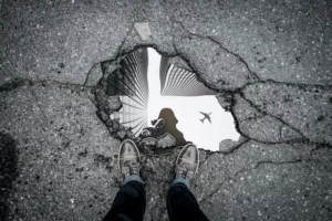 black and white shot of a pothole filled with water and reflecting an aeroplane in the sky