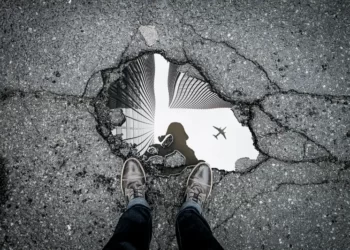 black and white shot of a pothole filled with water and reflecting an aeroplane in the sky