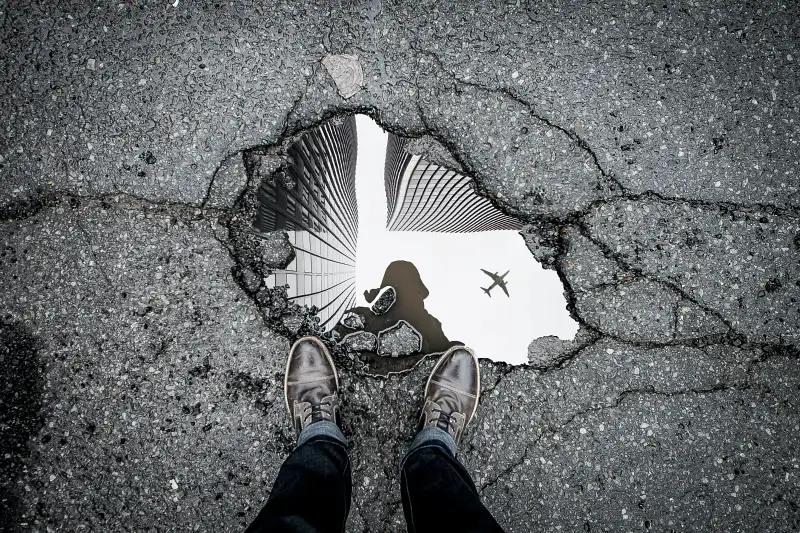 black and white shot of a pothole filled with water and reflecting an aeroplane in the sky