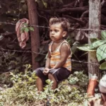 a young boy livingin structural poverty sat on a barbed wire fence