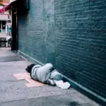A homeless man sleepingo n the ground in an alleyway