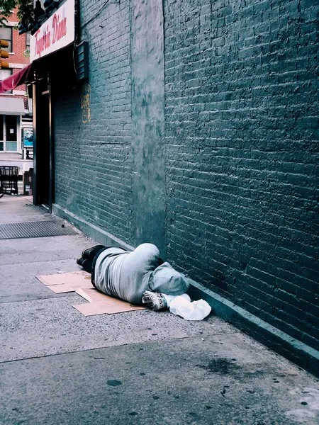 A homeless man sleepingo n the ground in an alleyway
