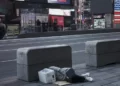 A homeless man asleep next to the road with a bucket on his head