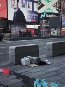 A homeless man asleep next to the road with a bucket on his head