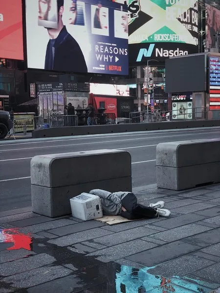 A homeless man asleep next to the road with a bucket on his head