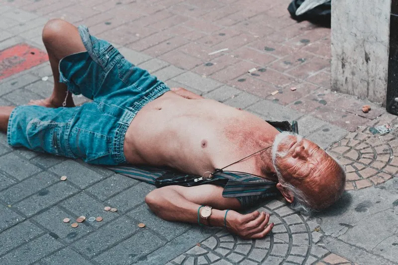 A homeless man laid out on a cobbled floor with no shirt on experiencing accumulation by dispossession