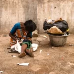 A woman on the street hiding her face. sat next to some rubbish bags. poverty
