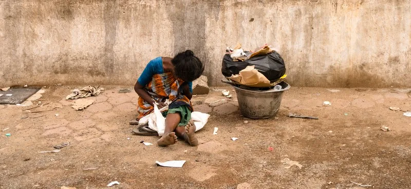 A woman on the street hiding her face. sat next to some rubbish bags. poverty