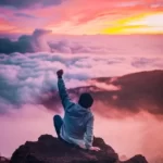 A man sat atop a mountain punching the air with his fist