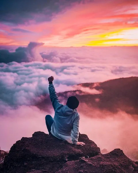 A man sat atop a mountain punching the air with his fist
