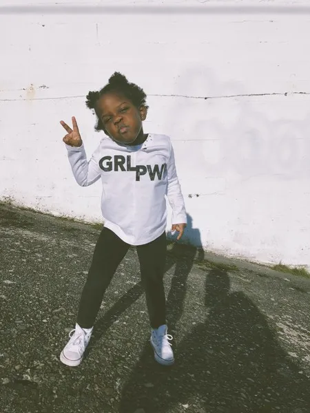 A young black girl wearing a tshirt which reads 'grl pwr'.