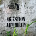 Grafitti on a grey wall which reads 'question authority'