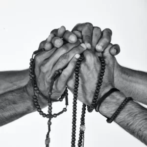 Black and white image of four hands intertwined with rosary beads