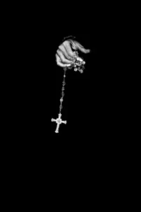 A hand holding a cross necklace against a black background