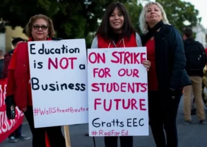 A group of teachers on strike with placards stating: education is not a business and on strike for our students future.
