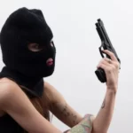 A woman dressed as an armed robber with balaclava and gun - symbolic violence and gender