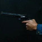 A hand holding an old style revolver gun against a black background