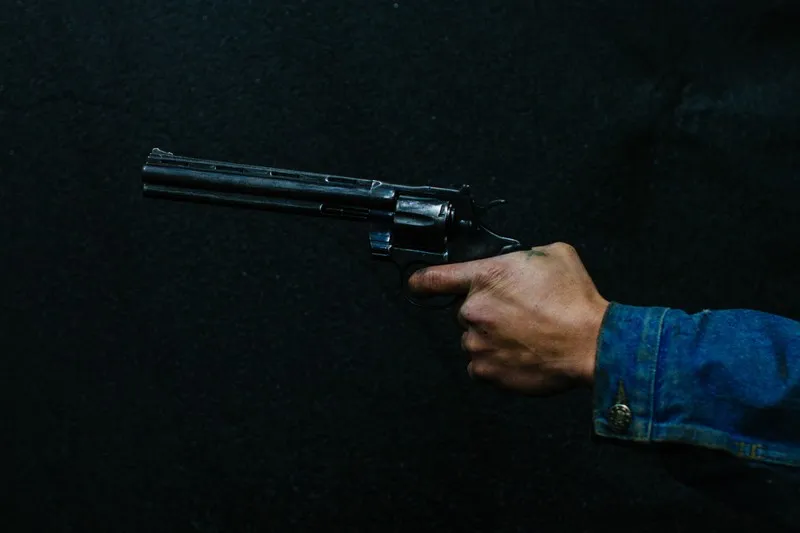 A hand holding an old style revolver gun against a black background