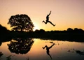 A silhouette of a person jumping through the air at sunset and reflected in a body of water