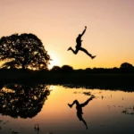 A silhouette of a person jumping through the air at sunset and reflected in a body of water