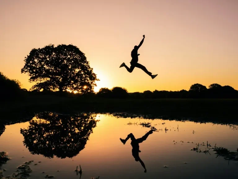 A silhouette of a person jumping through the air at sunset and reflected in a body of water