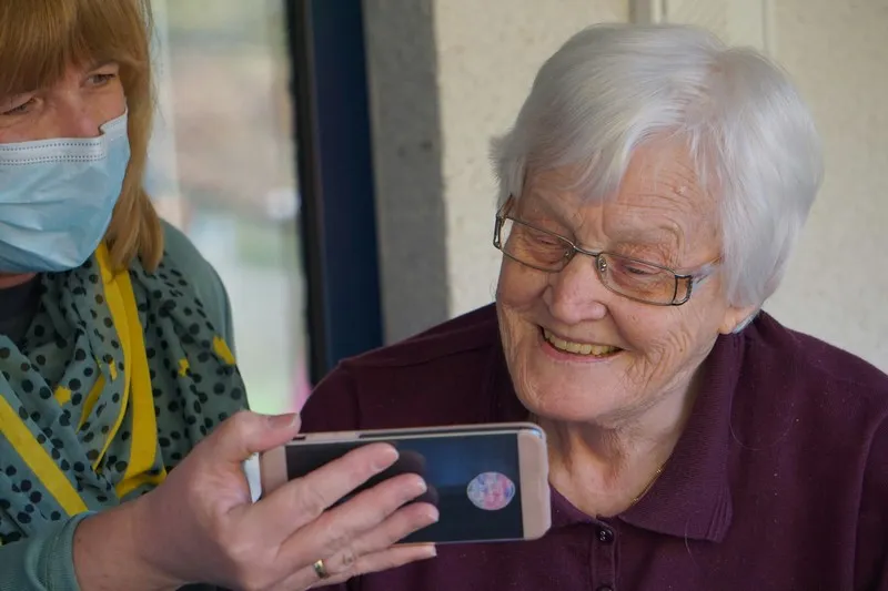 A carer helping to keep an older person entertained with a phone