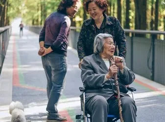 An aging woman in a wheelchair on a sunny day. She is surround by trees and shade.