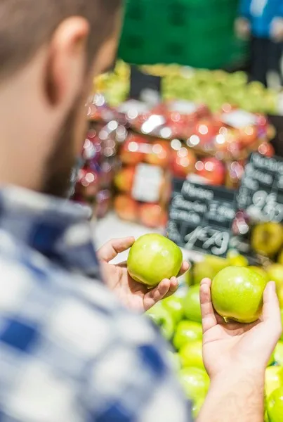 A man holding two apples the same indicating the lack of consumer choice