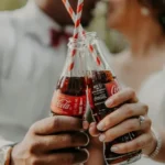 Two people holding two bottles of coca-cola with striped straws - cola-isation