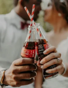 Two people holding two bottles of coca-cola with striped straws - cola-isation