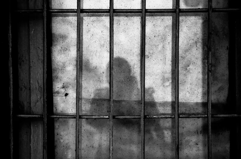 the silhouette of a person behind bars in a jail cell