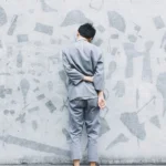 A man in a grey outfit facing a wall and facing discipline