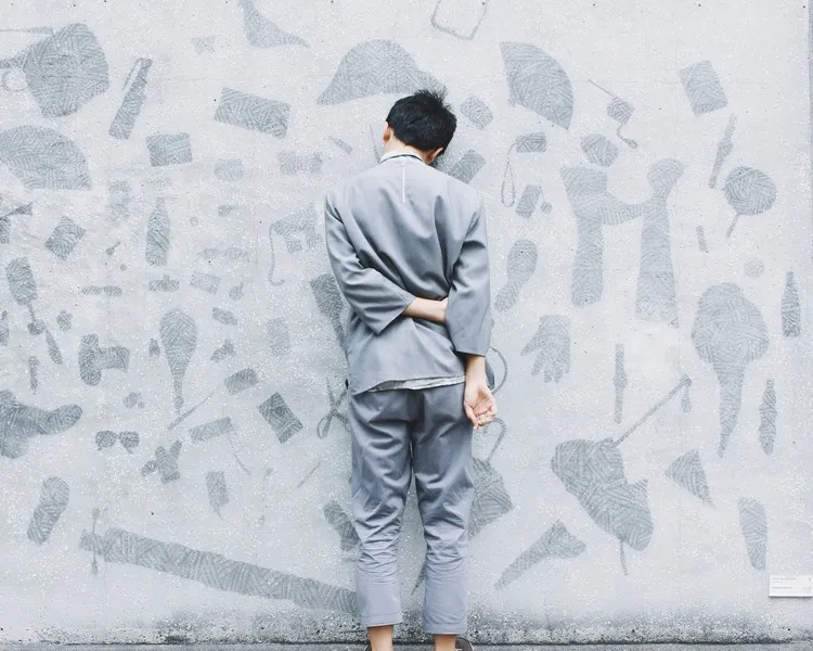 A man in a grey outfit facing a wall and facing discipline