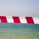 A line of red and white tape separating sky from beach to indicate taboo, censorship, or forbidden