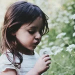 A young girl blowing a flower