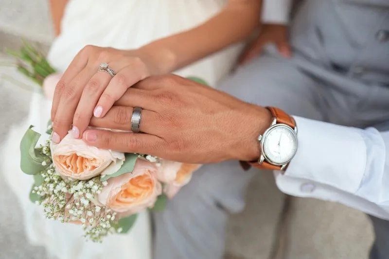 A couple engaging in conjugal roles by getting married. Hands are visible with wedding rings and flowers.