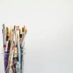 A selection of paintbrushes in a glass against a grey background