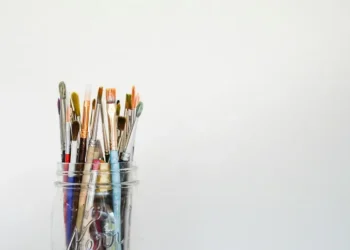 A selection of paintbrushes in a glass against a grey background