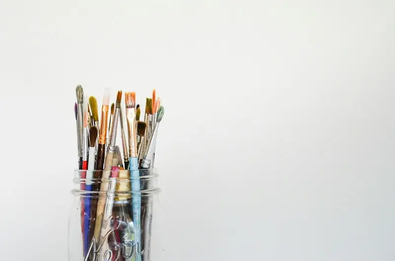 A selection of paintbrushes in a glass against a grey background