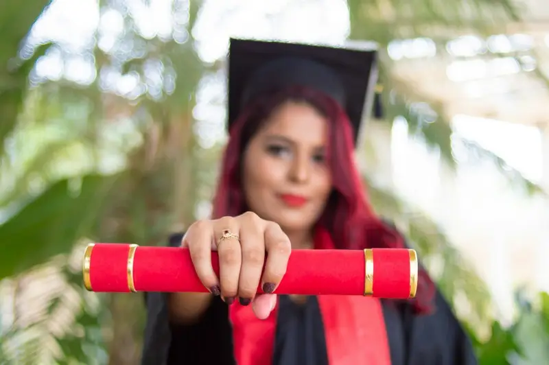 A females university graduate holding her credentials to the camera
