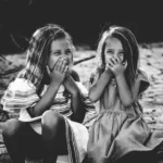A black and white shot of two girls giggling behind their hands