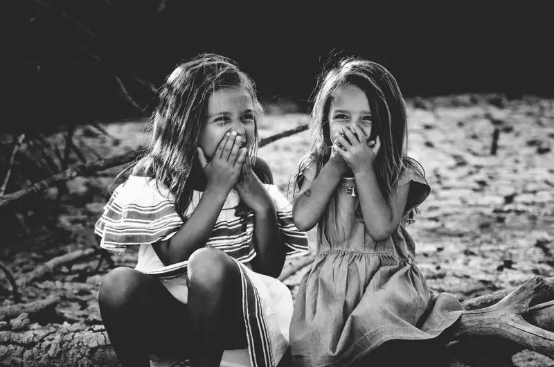 A black and white shot of two girls giggling behind their hands