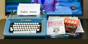 A typewriter typing out the words 'fake news' alongside some books with the same title