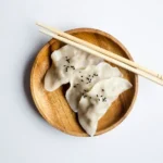 three gyoza on a wooden plate with chopsticks