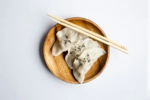 three gyoza on a wooden plate with chopsticks